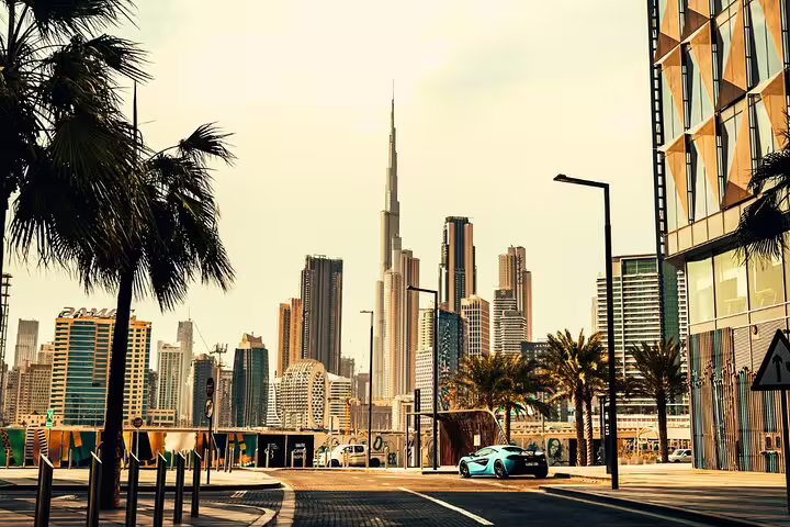 Dubai skyline with Burj Khalifa towering over modern architecture, viewed from a palm-lined street on a sunny day.