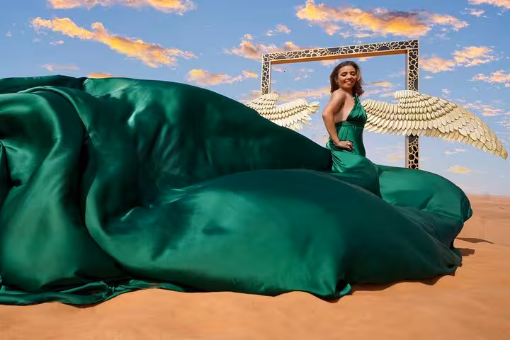 Elegant woman in a green dress with angel wings stands in Dubai's desert, part of the flying dress photography experience.