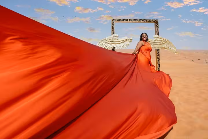 Woman in vibrant red dress with golden wings in Dubai desert on flying dress photography tour.