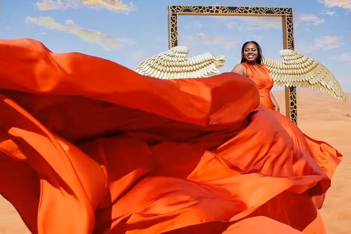 Elegant woman in red dress and golden wings in Dubai desert, enjoying flying dress photography experience.
