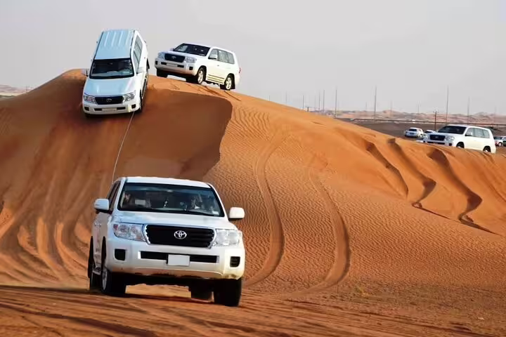 Convoy of 4x4 vehicles navigating the majestic sand dunes during a Dubai desert safari.