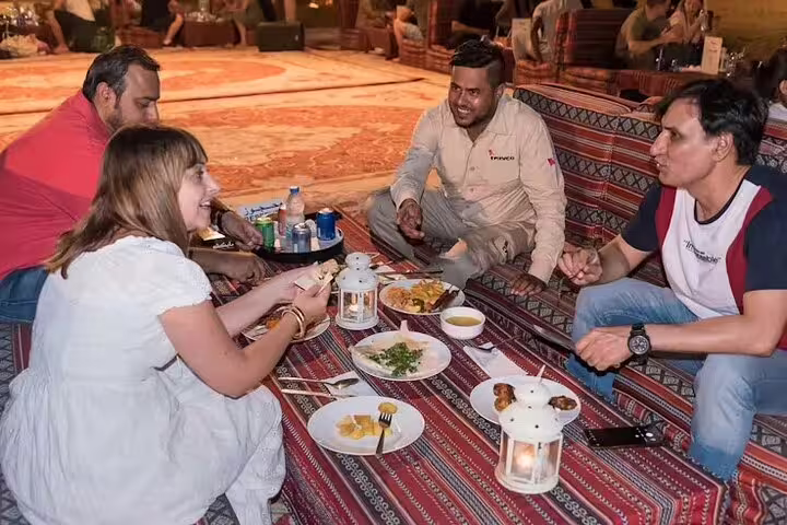 Tourists dining on carpets with Emirati host, enjoying BBQ dinner and Arabic hospitality on a Dubai desert safari