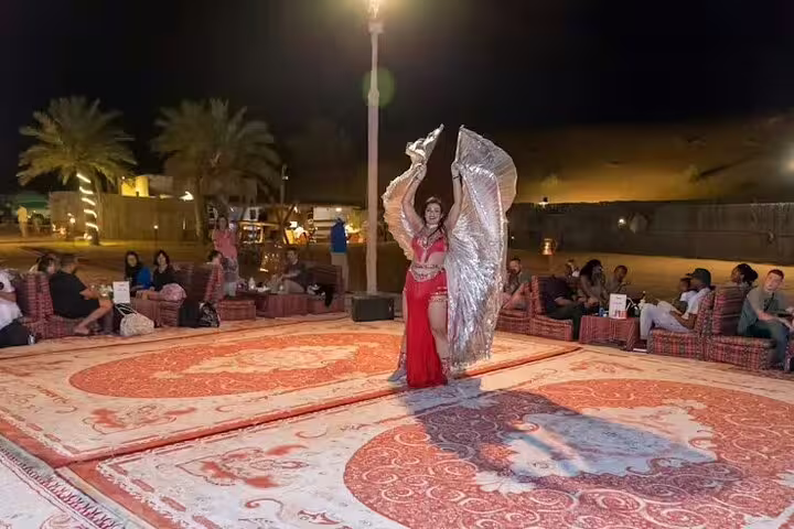 Belly dancer performing with silver wings on open-air stage at Dubai desert safari camp with guests seated around