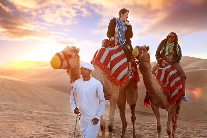 Two people enjoying a camel ride at sunset in the Dubai desert during a premium safari tour.