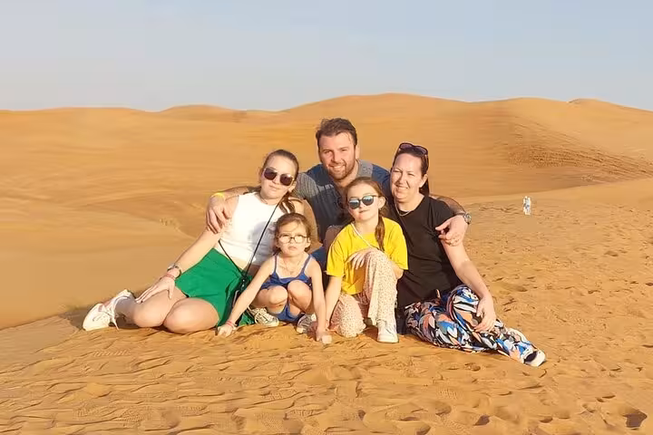 Family posing on golden dunes at Dubai desert safari sunset after quad bike ride, camel trek and BBQ dinner
