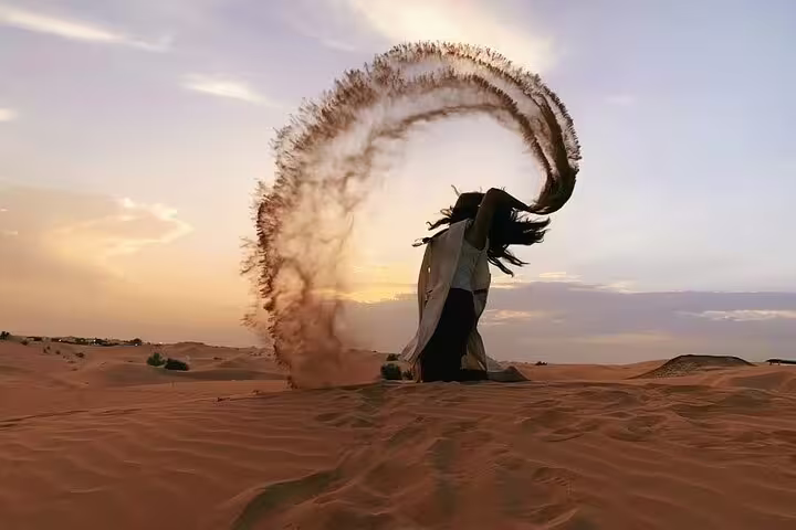 Traveler enjoying a scenic sunset in the Dubai desert, creating a dramatic sand splash.