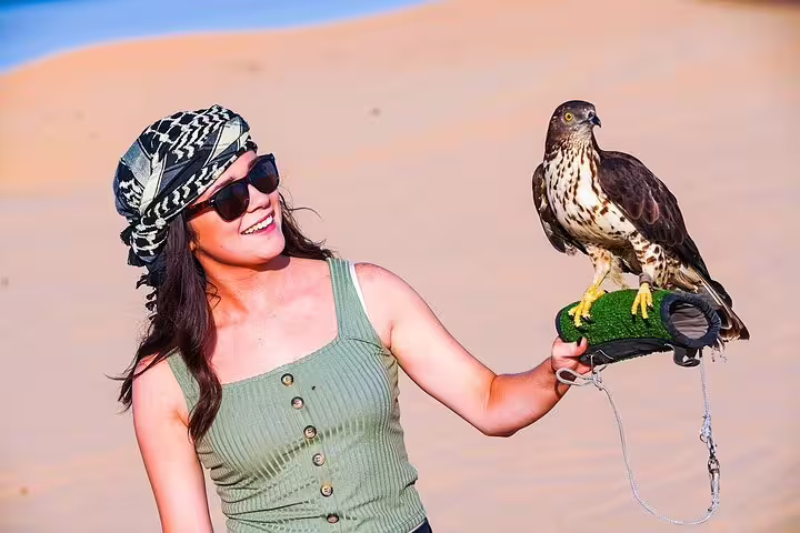 Smiling tourist holding a falcon during a Dubai desert safari experience.