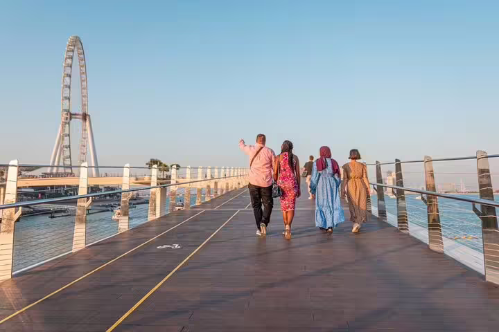 Small group on Dubai Marina guided walking tour crossing a waterfront boardwalk near Ain Dubai with sea views at sunset