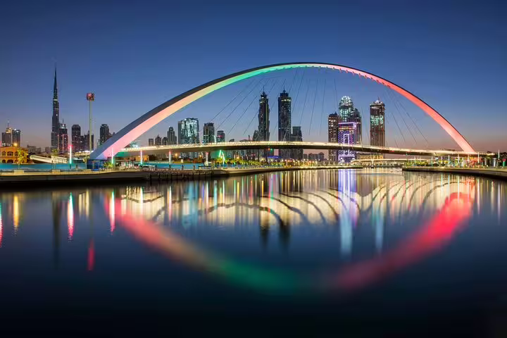 Dubai skyline at dusk with illuminated bridge reflecting on water, perfect for a magical day and night tour.