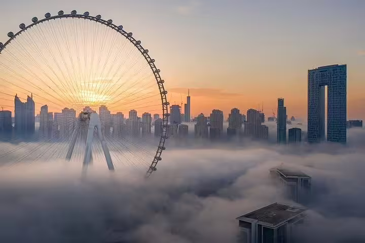 Dubai skyline at sunrise with iconic Ferris wheel emerging through morning fog on a full-day city tour.