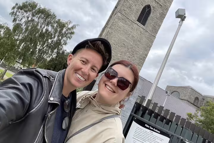 Two smiling women taking a selfie in front of St. Audoen's Church tower in Dublin