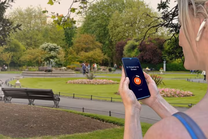 Woman holding phone with audio guide app at St Stephen's Green park in Dublin