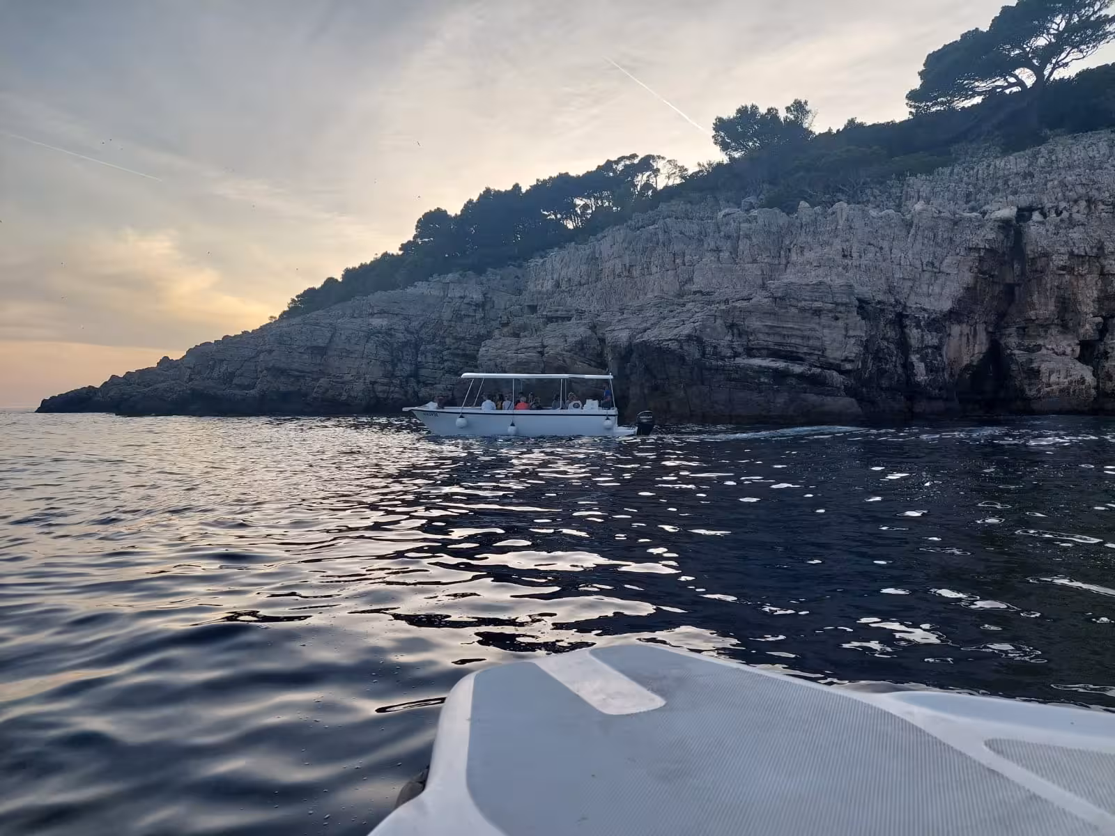 Small boat cruising past rocky Adriatic cliffs at sunset on Dubrovnik panorama by boat sightseeing tour