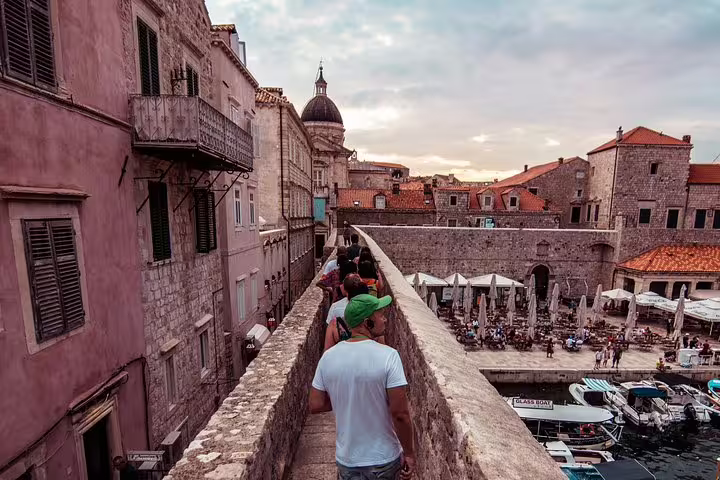 Guests stroll Dubrovnik city walls above Old Town harbor at sunset on Ancient City Walls & Wars walking tour