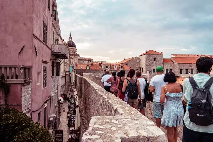 Tourists walking Dubrovnik Old Town ramparts past stone fortifications on Ancient City Walls & Wars tour route