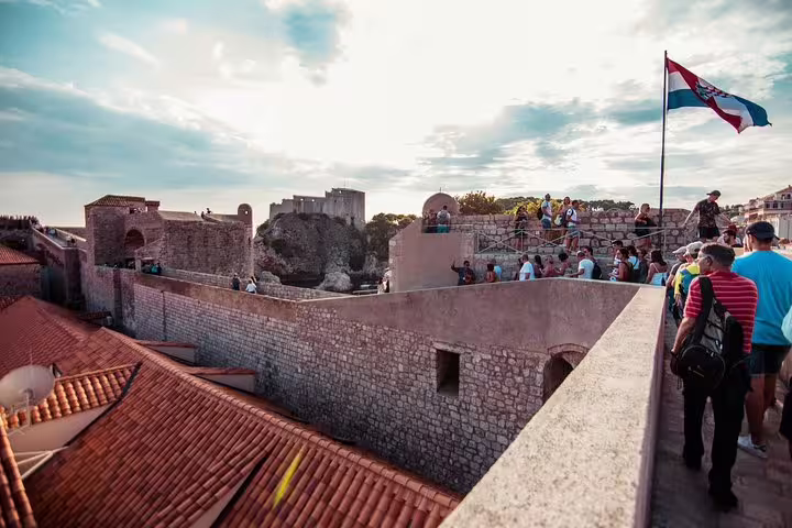 Group walking along Dubrovnik fortress walls with Croatian flag, Ancient City Walls & Wars walking tour view