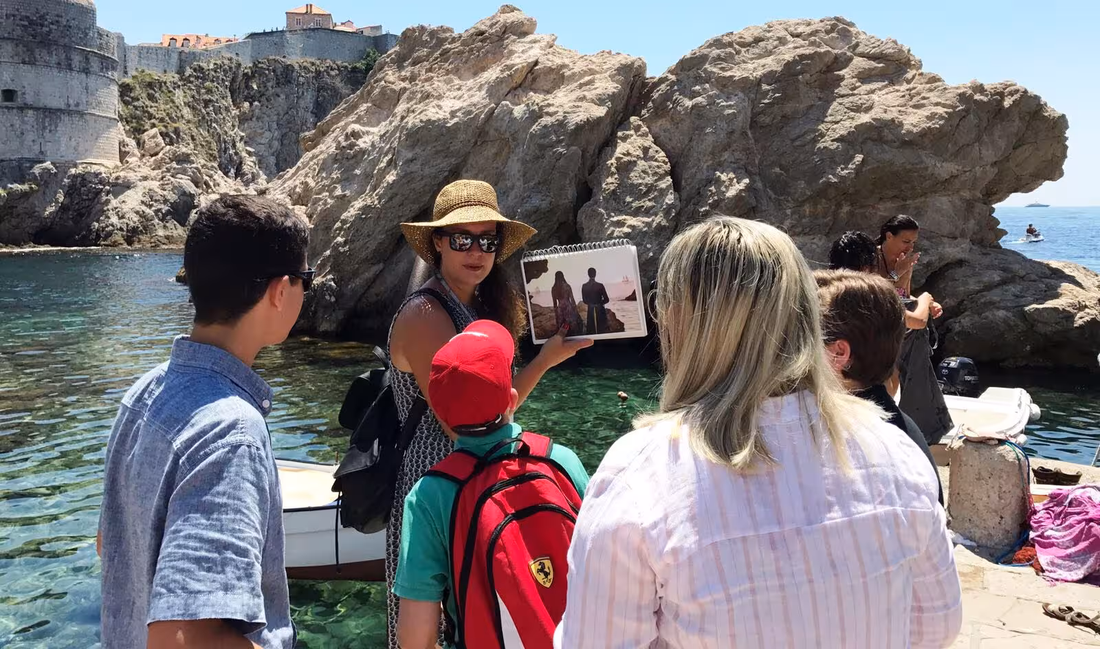 Small group at Dubrovnik West Harbor as guide shows Game of Thrones scene book on combo GOT and history walking tour