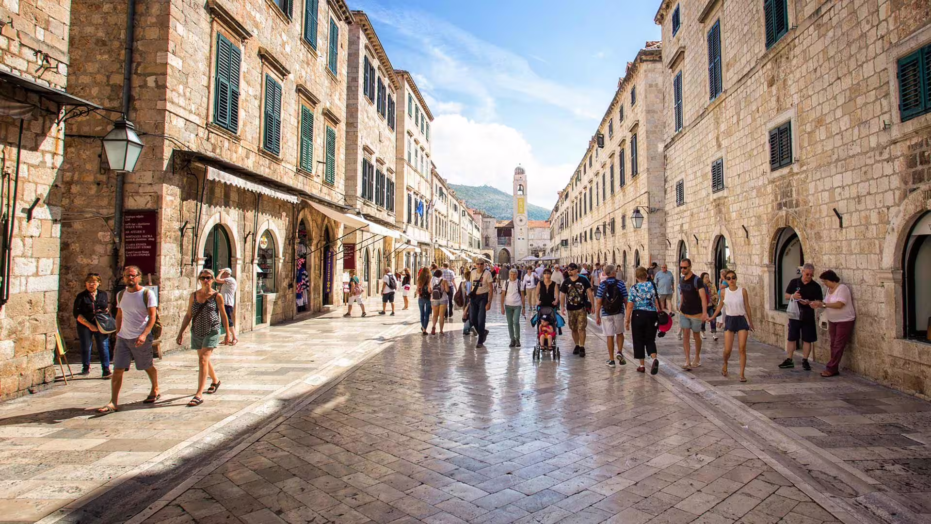 Guided Old City group walking tour along Dubrovnik’s Stradun, passing historic stone buildings and bell tower