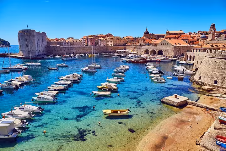 Dubrovnik Old Town harbour with crystal clear turquoise water, moored boats, and historic stone walls and buildings