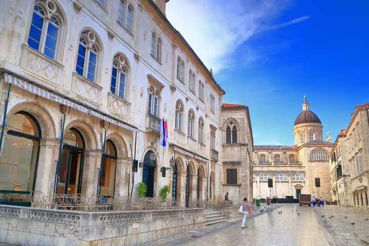 Historic Dubrovnik old town square with white stone buildings and cathedral dome under blue sky