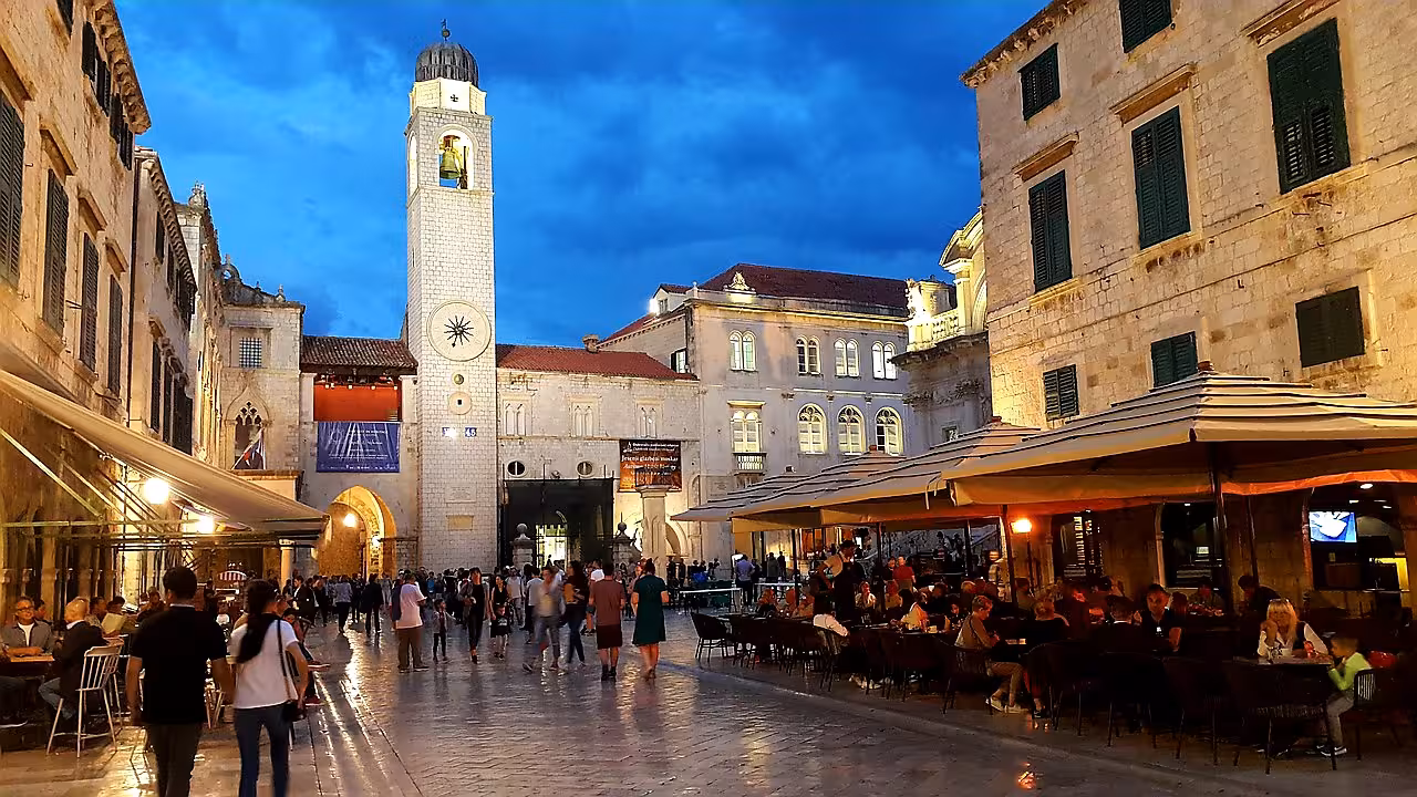 Evening in Dubrovnik Old Town on Stradun with clock tower and cafés, part of the history by night tour