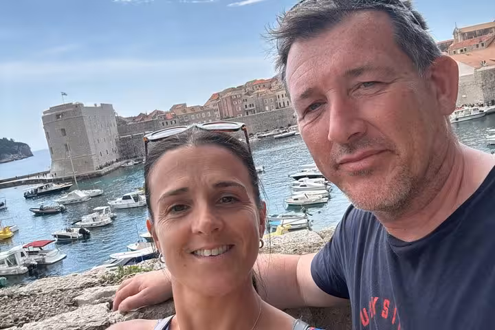 Couple smiling at Dubrovnik Old Town harbour with boats and medieval fortress walls in background