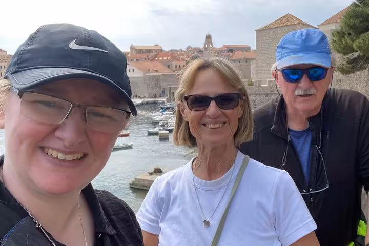Three tourists smiling during a walking tour of Dubrovnik Old Town with harbor and historic walls behind them