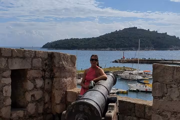 Woman in pink dress posing with historic cannon on Dubrovnik Old Town walls overlooking harbor and Lokrum Island