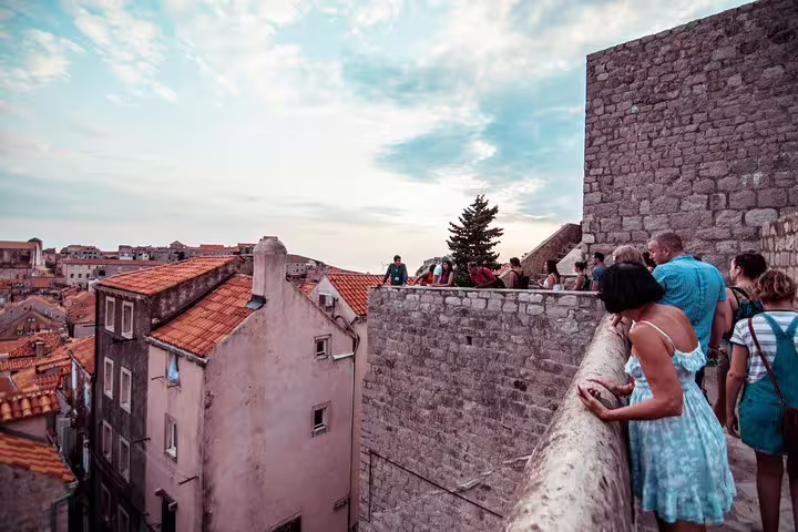 Visitors on Dubrovnik old town walls overlooking red rooftops at sunset on Ancient City Walls & Wars walking tour