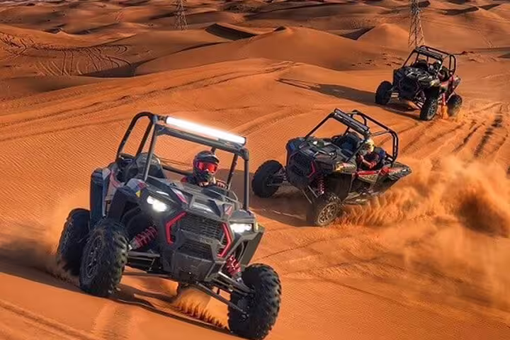 Three dune buggies race across the golden sands of Dubai desert, showcasing thrilling adventure and excitement.