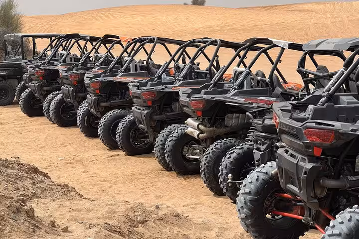 Line of off-road dune buggies beside rolling sand dunes, set for desert safari quad bike ride and dune bashing