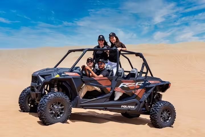 Group enjoying a thrilling dune buggy ride in the Dubai desert under a clear blue sky, perfect for adventure seekers.
