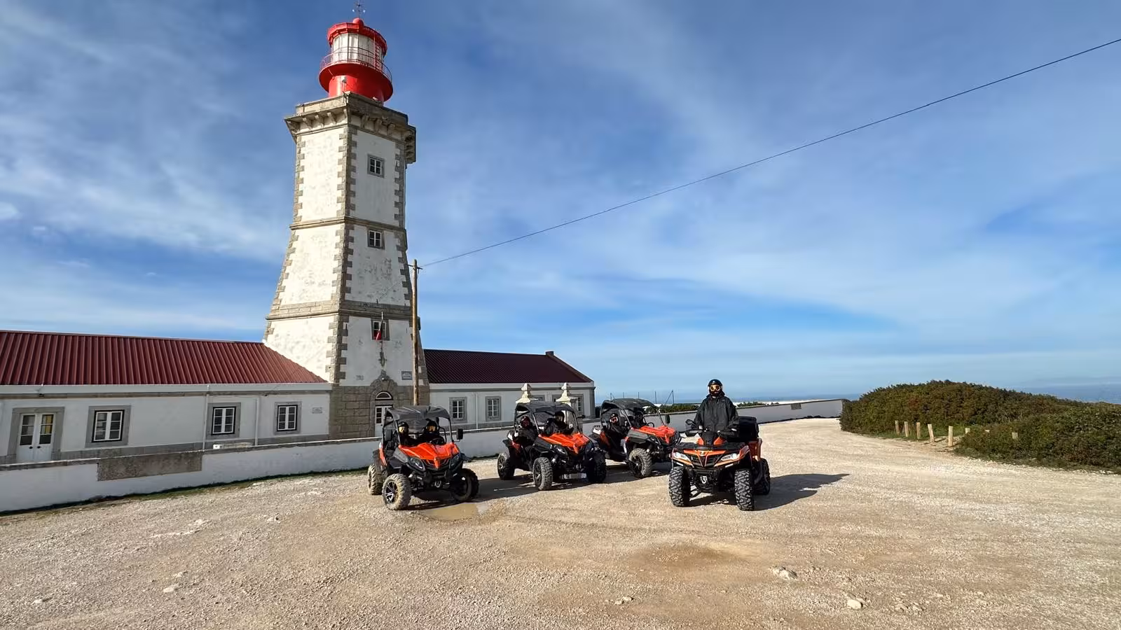 Dust Breaker buggy tour group with off-road UTVs parked by a coastal lighthouse viewpoint under blue skies