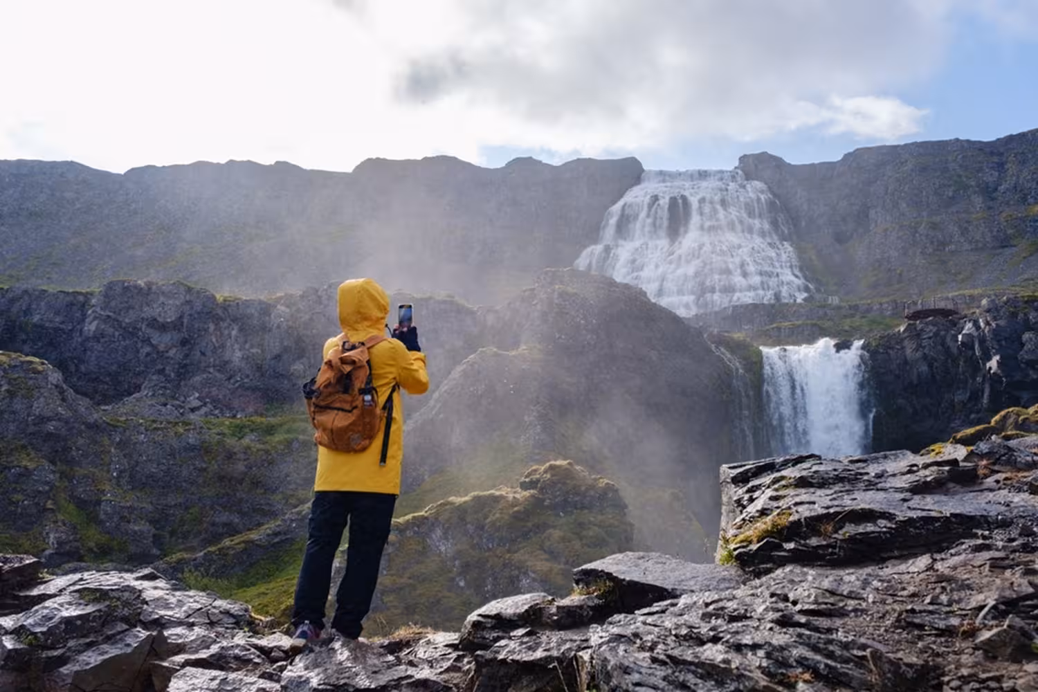 Hiker in yellow jacket photographing Dynjandi waterfall in Iceland's Westfjords on a misty day