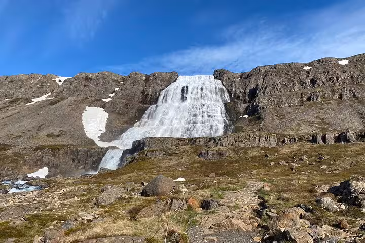 Dynjandi waterfall cascading down rocky cliffs in Iceland's Westfjords with snow patches and blue sky