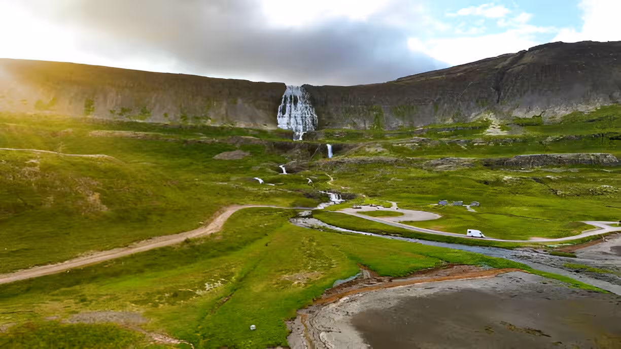 Aerial view of Dynjandi Waterfall cascading down green cliffs in Iceland's Westfjords with a campervan on a winding road