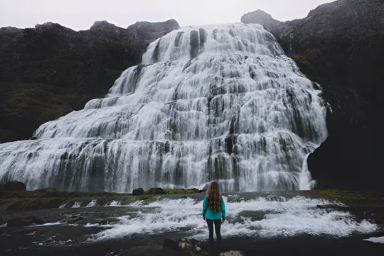 Woman standing before the cascading tiers of Dynjandi Waterfall in Iceland's Westfjords