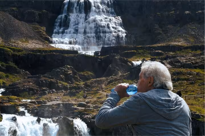 Traveler drinking water bottle with Dynjandi waterfall cascading down rocky cliffs in Westfjords Iceland