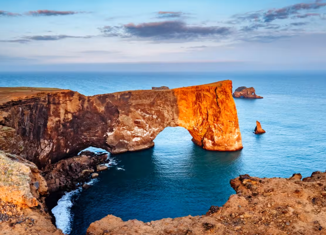 Dramatic Dyrholaey rock arch on Iceland South Coast tour with golden volcanic cliffs overlooking the Atlantic Ocean