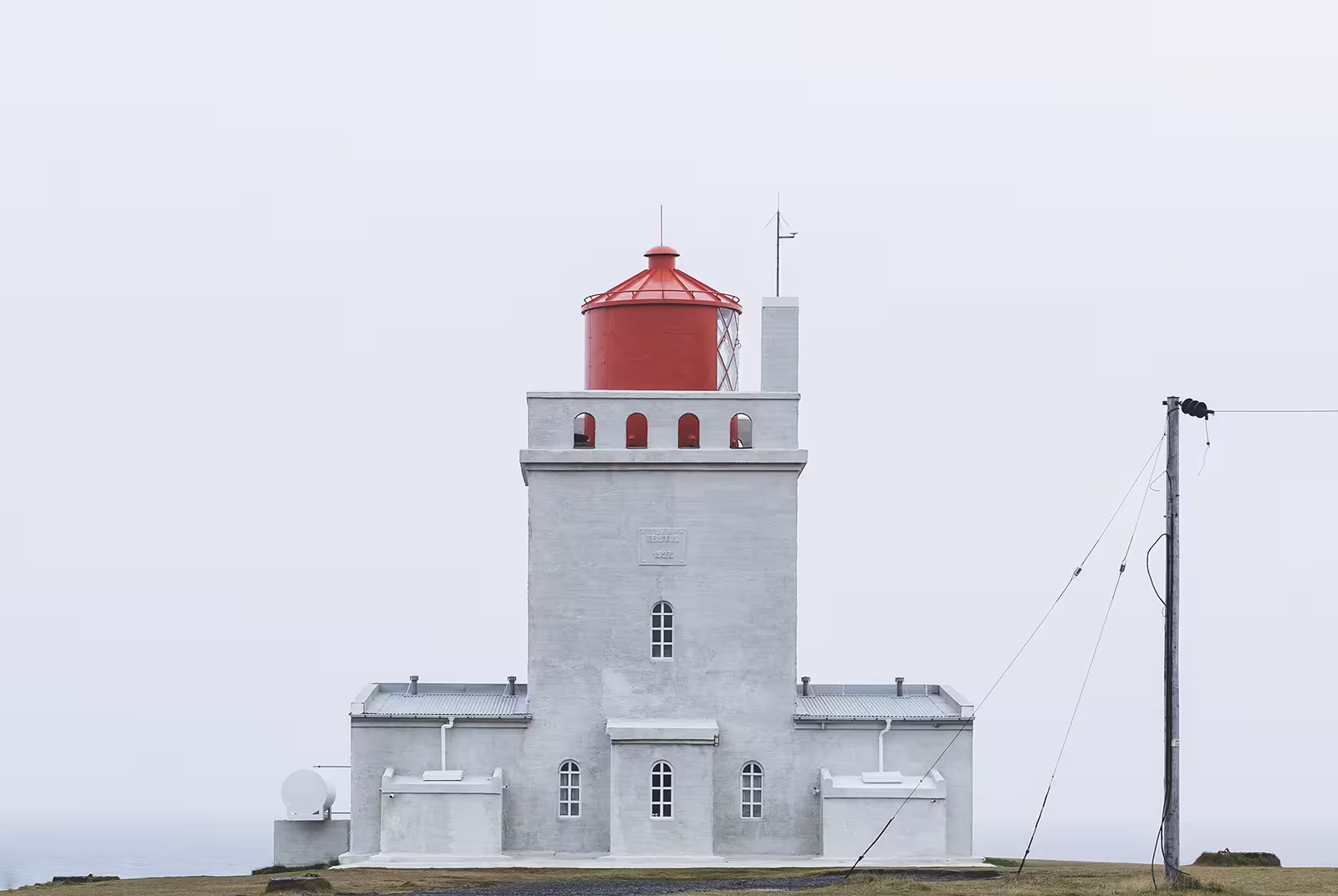 White lighthouse with red lantern room on Iceland's south coast under overcast sky