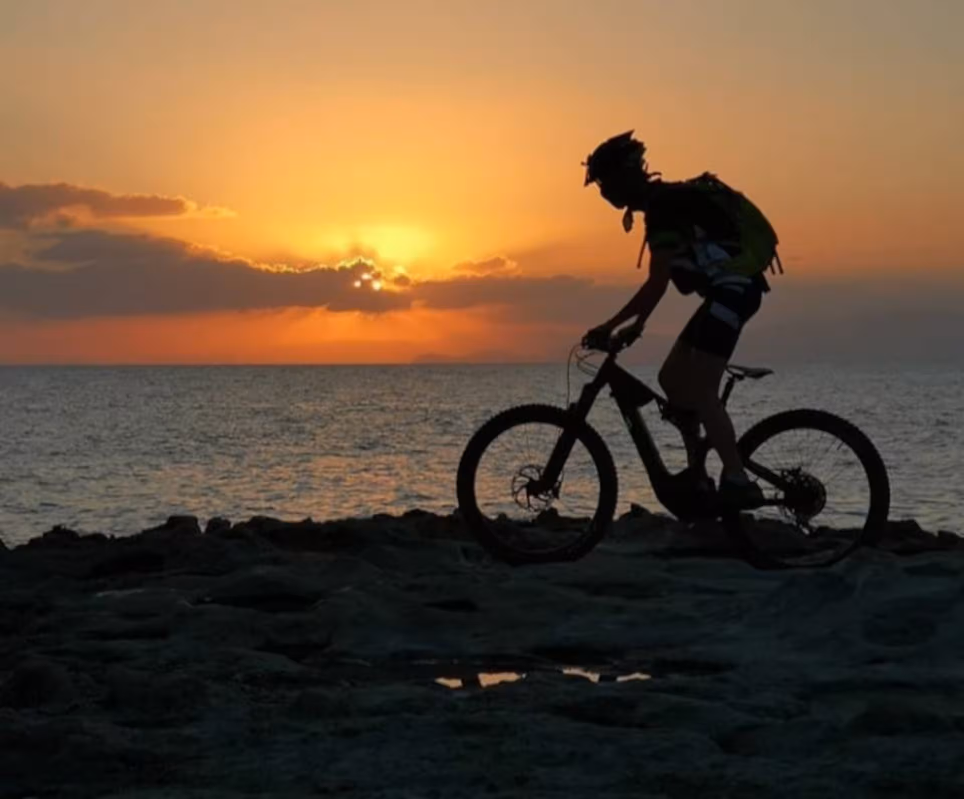 Cyclist enjoying a sunset ride along the Alghero coastline on an e-bike tour, silhouetted against the vibrant sky.