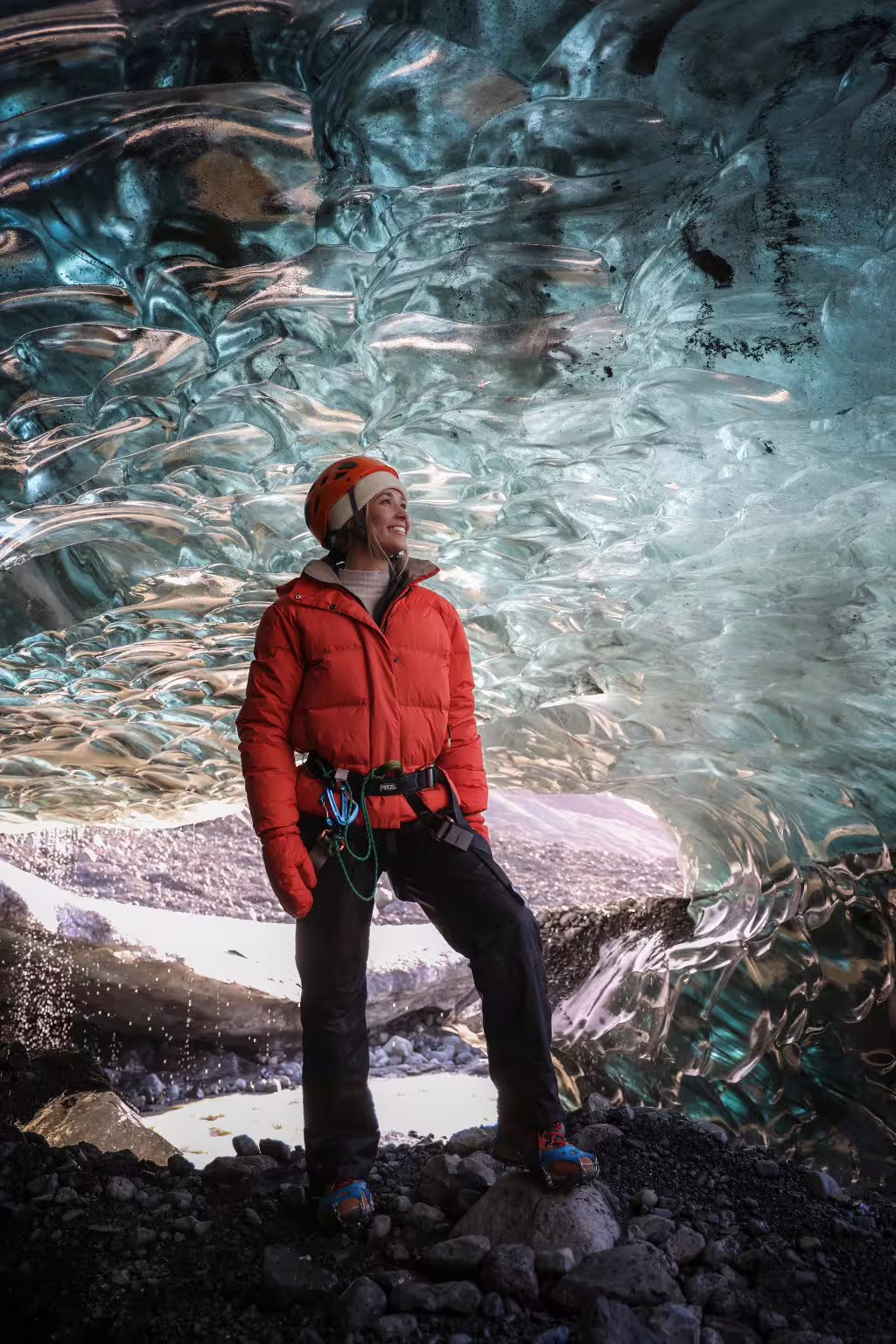 A smiling woman in a red jacket and helmet stands inside a stunning sapphire ice cave in Iceland on an early bird guided tour.
