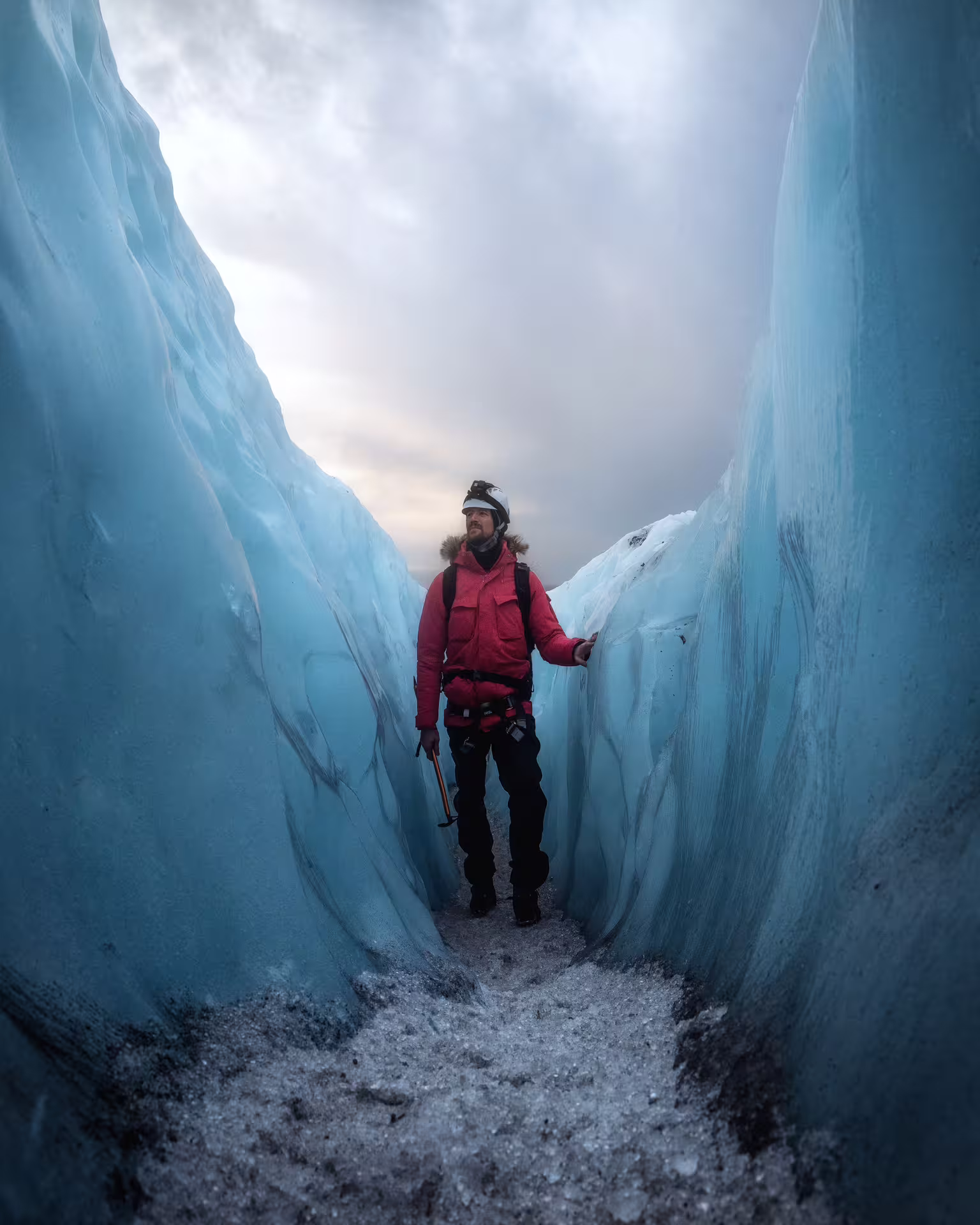 A guide in a red jacket navigates a narrow sapphire ice cave crevasse on an early bird Iceland glacier tour