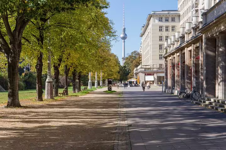 Tree-lined boulevard in East Berlin with Fernsehturm TV tower visible in background on sunny autumn day