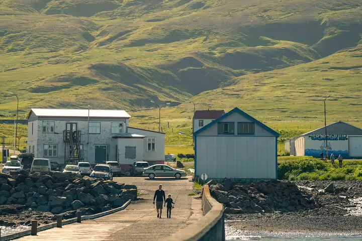 Two people walking along a coastal path in a small East Iceland village with green mountains behind