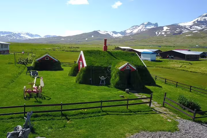 Traditional Icelandic turf houses with grass roofs in East Iceland, snow-capped mountains in background