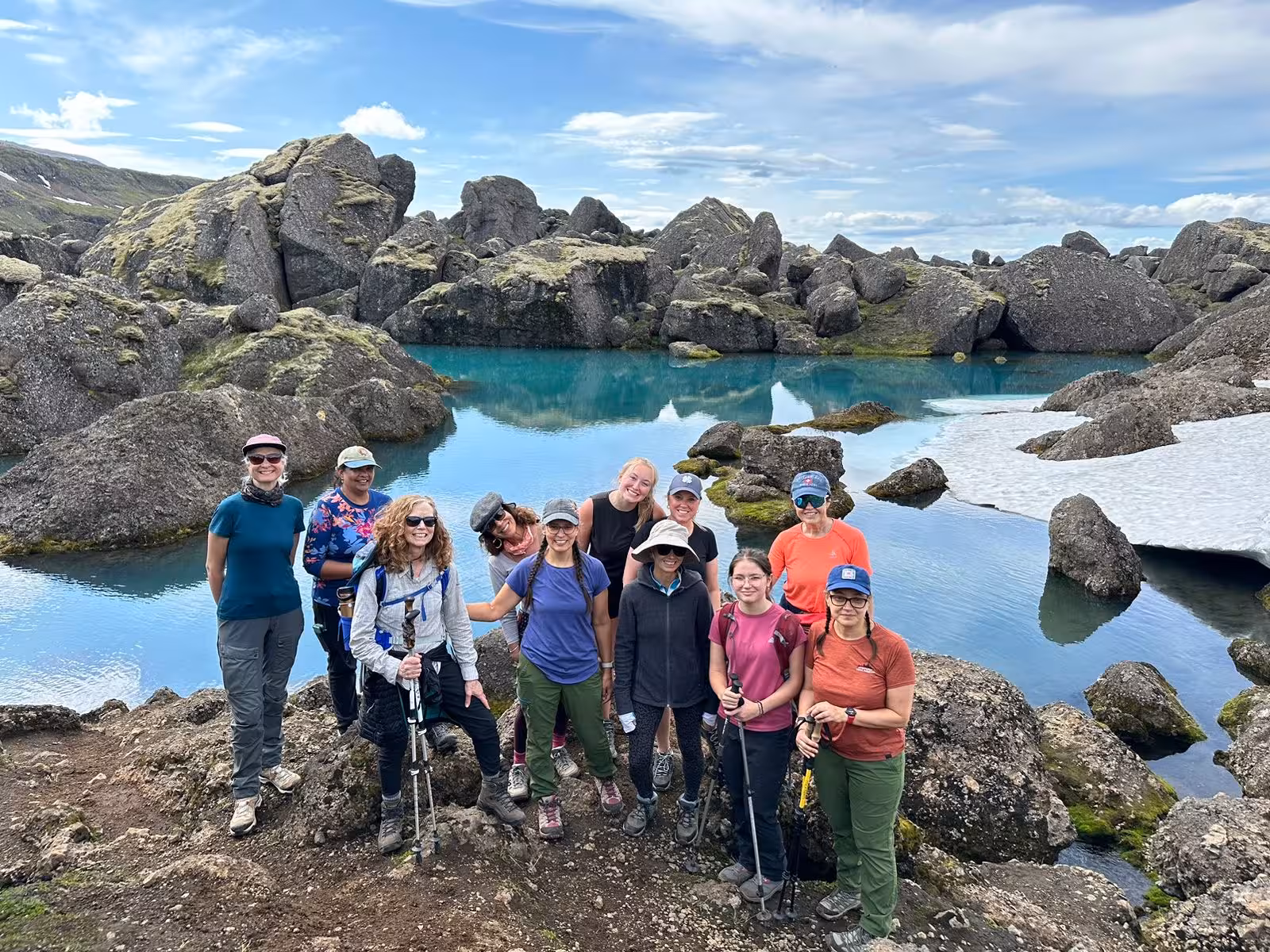 Guided hiking group posing beside a stunning turquoise glacial lake surrounded by rugged rocks in East Iceland remote fjords