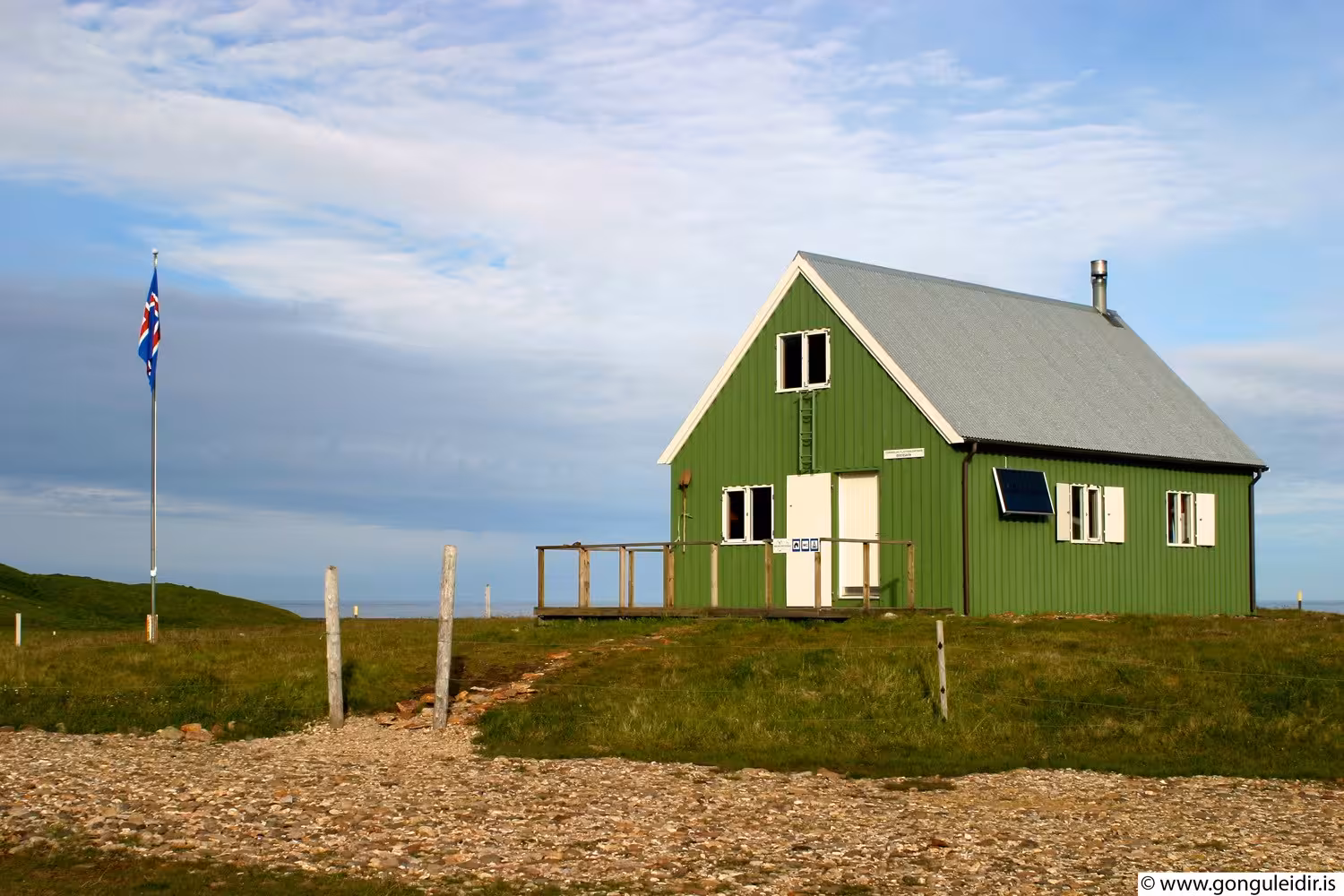 Remote green Icelandic hiking hut with Iceland flag in East Iceland fjords landscape under blue sky