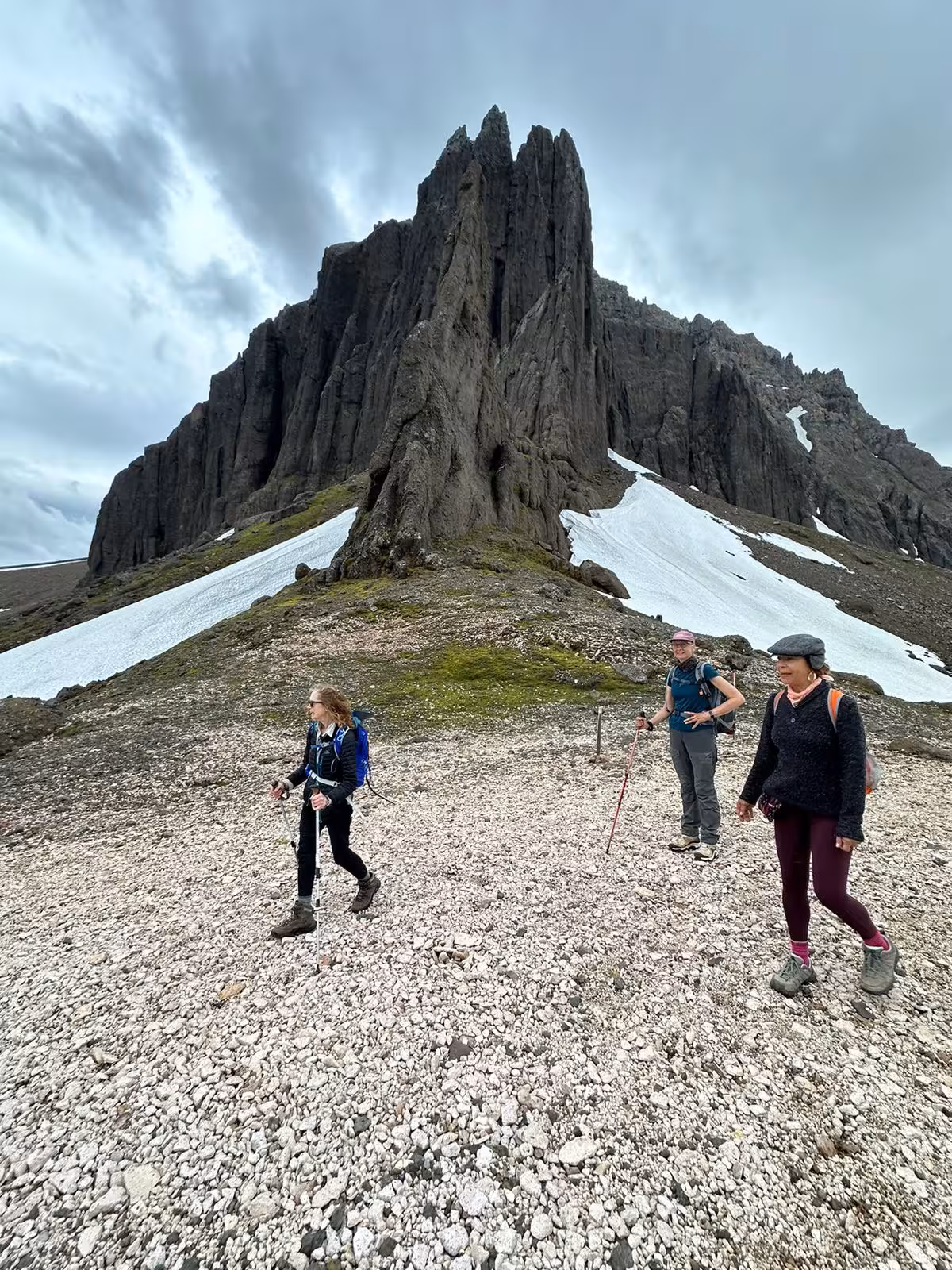 Three hikers trekking rocky terrain below dramatic jagged peaks with snow on a guided East Iceland fjords tour
