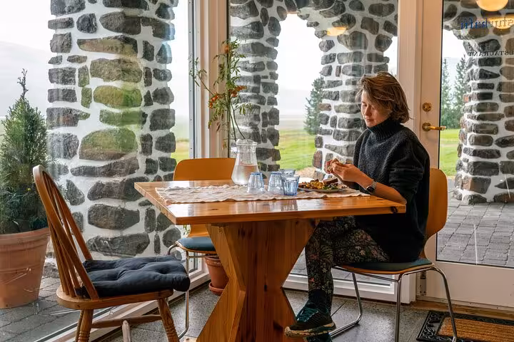 Woman dining alone at wooden table in stone-walled restaurant with scenic East Iceland landscape view